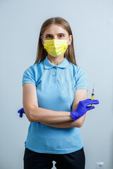 A young woman is an intern doctor, she is in a blue T-shirt and medical gloves and holds a syringe in her hand, a protective mask is on her face. Nurse with a vaccine in her hands. selective focus