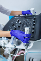 A close-up of the hands holding the ultrasonic probe of an ultrasound machine on which a special gel is applied. selective focus
