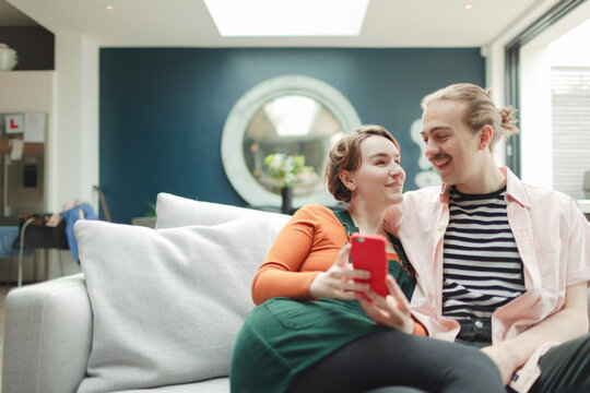 Happy couple with smart phone on living room sofa