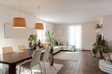 Large living room with dining table, light chairs and a large sofa. Large bright windows