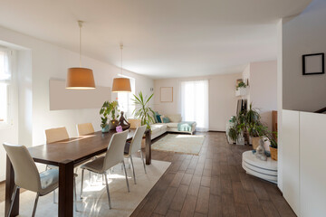 Large living room with dining table, light chairs and a large sofa. Large bright windows