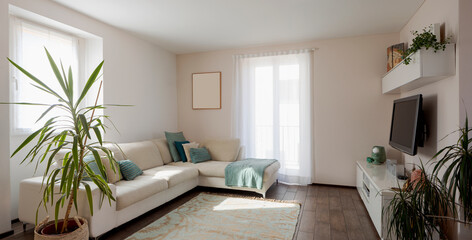 Living area with large bright windows, fabric sofa with colored cushions and a cabinet with television