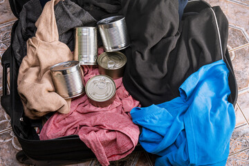 Clothes and cans are in the suitcase. Concept - collection of things during a natural disaster,...