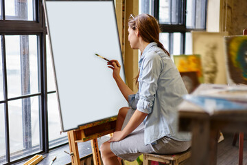 Casual dressed female artist with paintbrush drawing abstract paintings on canvas have workshop at...