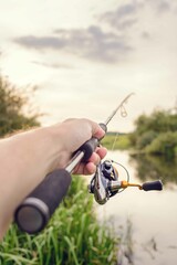 Male hand holds spinning rod on the background of the river.