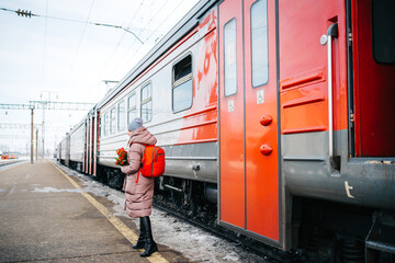 girl on the platform of the station with a red backpack and a bouquet of tulip flowers