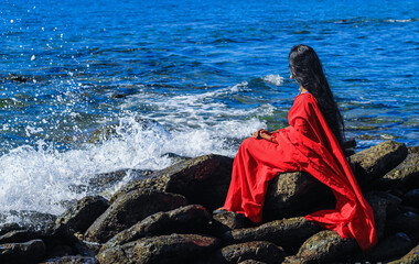 Young women wearing a red saree on the beach. Girl in traditional Indian sari among the rocks and...