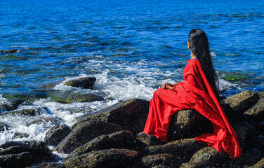 Young women wearing a red saree on the beach. Girl in traditional Indian sari among the rocks and...