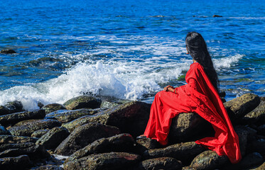 Young women wearing a red saree on the beach. Girl in traditional Indian sari among the rocks and enjoying the freedom and the sunset or sunrise. Beautiful Indian woman on the beach wearing a sari.