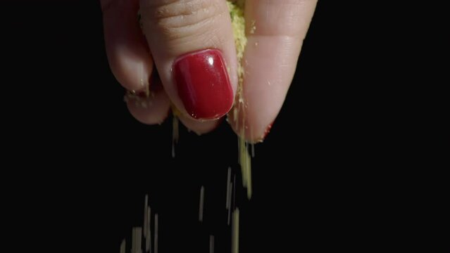 A pinch of spices for cooking in a woman's hand. A woman sprinkles fragrant spices on a black background. Macro shooting. Slow motion.