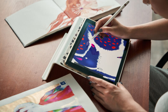 Female illustrator sitting at the table and drawing creative pictures at the tablet