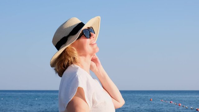 happy 50 year old woman in straw hat and sunglasses enjoying the sun against the blue sea background. Summer, vacation, vacation, active retirees