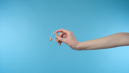 Woman holding hearing aid equipment on blue background