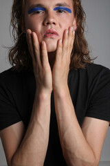 Vertical close-up portrait of a young man with make up and long hair in studio.