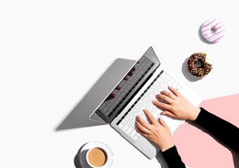 Person using a laptop computer with a donut and a cup of coffee - Flat lay - Powered by Adobe