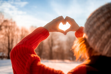 Love wintertime woman hands making heart shape during beautiful winter sunset