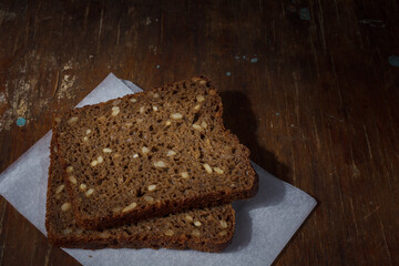 Russian Borodinsky or borodino bread, dark brown sourdough rye bread, two slices with sunflower seeds on parchment paper on wooden table. Copy space