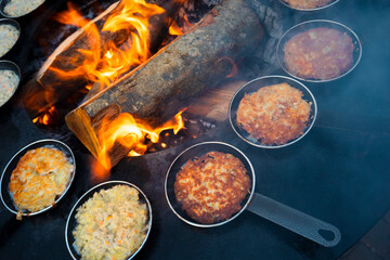 Potato pancakes are fried in small pans over an open fire. Treats at the fair on an iron stove and open fire on logs. Latvia