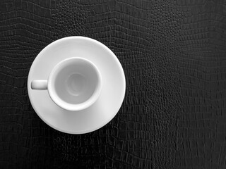Empty white ceramic coffee cup and saucer on black table, top view
