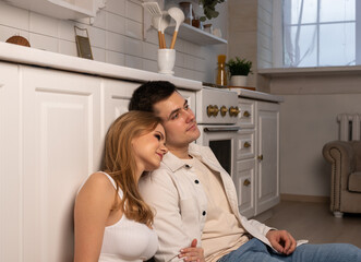 Happy young couple sitting on floor in modern white scandi kitchen. Tender and loving relationship concept. High quality photo