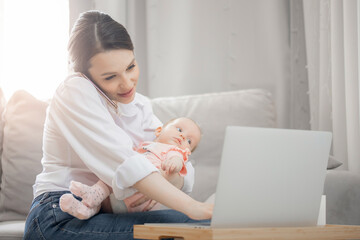 Concept freelance life style maternity leave. Beautiful young mother with baby girl working at home office using laptop computer, sun light
