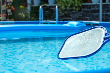 Pool Skimmer Net against clear blue water in a pool with an inflatable mattress. Round frame pool and leaf netting skimmer for cleaning leaves from the surface of the water.
