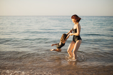 Mother and daughter on sea rest. Family are on sea beach. Mom and daughter in black swimwear playing on sea water. Woman with girl swimming and splashing in sea.