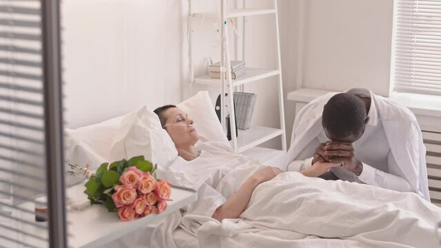 Medium slowmo of upset Black man vising his sick wife at hospital. Woman with oxygen tube in her nose sleeping in hospital bed
