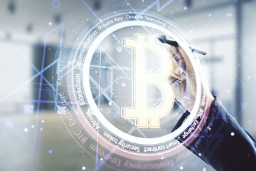 Double exposure of male hand with pen working with creative Bitcoin symbol hologram on blurred office background. Mining and blockchain concept