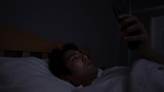 Holiday concept of 4k Resolution. Young Asian man playing mobile phone in bedroom.