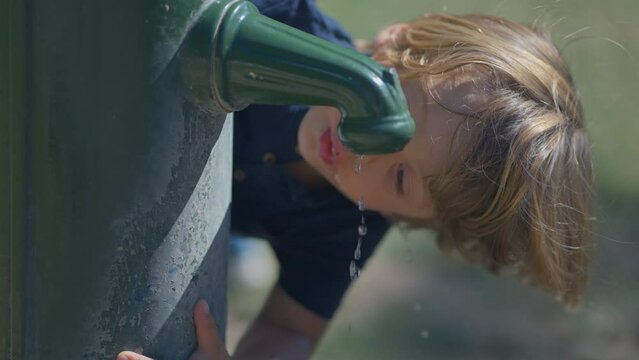 Child drinking water from public water faucet outside