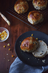Close up angle view of Easter theme food image shot from above. Freshly baked and served on a plate hot cross buns. Ingredients and baking tray in shot. Copy space available. Dark and vintage style