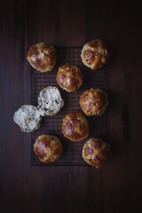 Fototapeta na wymiar Flat lay image of freshly baked hot cross buns arranged on a baking tray. One Easter bake has been torn open ready for butter or jam. Dark wood background with copy space.