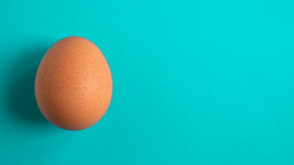 Brown spotted chicken egg on a blue background. Copy space. Flat lay. Minimal concept.