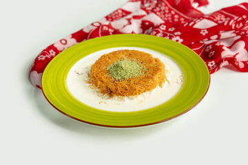Turkish dessert kunefe, kunafa, kadayif with pistachio with walnut powder in a dish isolated on colorful table cloth top view on grey background