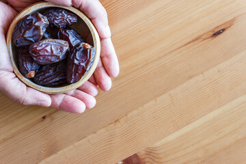 Top view of dry palm dates in wooden bowl on woman hand with copy space. Ramadan concept. Holy muslim month.
