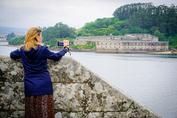 blonde young woman with blue coat taking photos at Castillo de San Felipe. Stone and earth coastal...
