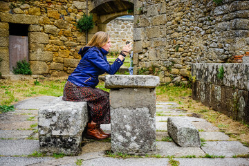 Beautiful young woman taking photos with her cell phone sitting on a stone bench