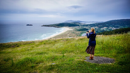 Fototapeta premium Young and beautiful woman taking photos with the mobile on the coast of Galicia