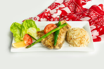 Grilled Sea Bass with rice and Greek salad in a dish isolated on colorful table cloth top view on grey background