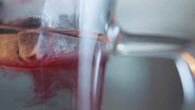 Macro shot of a fruit teabag diffusion in a glass cup. Tea leaves dissolve throughout the water, turning the water red.