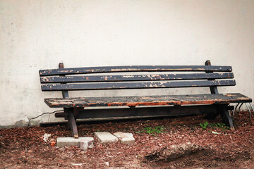 Old gray wooden bench standing on dry grass near plaster wall