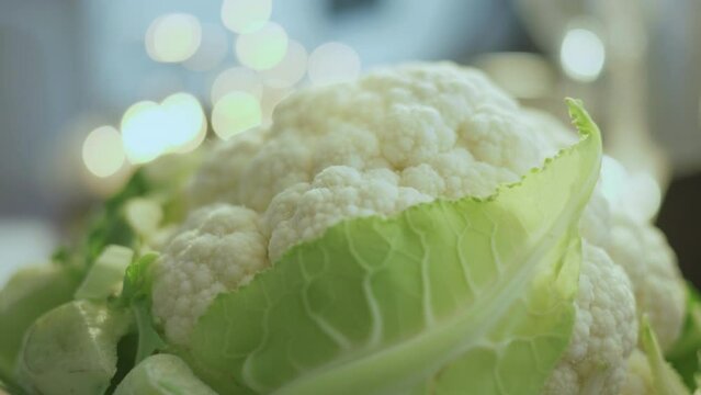 Macro shot of raw cauliflower with a white wholesome inflorescence and fresh green leaves.