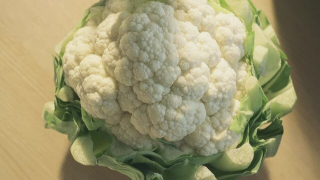 Beautiful fresh cauliflower, white head surrounded by green leaves, rotating on a wooden surface, close-up shot.
