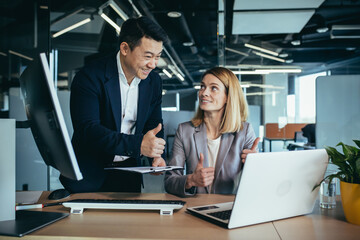 Naklejka premium two business people consulting on a project looking at computer monitor screen sitting in the office. Asian male employee Coworker explains colleagues ideas and strategies accountant, financial report