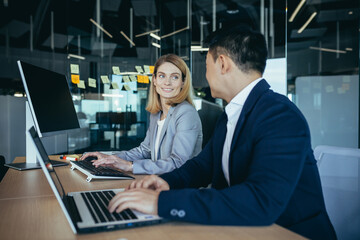 happy coworkers discuss project strategy by looking and pointing at laptop pc computer monitor screen. multiethnic business team in the office. confident mature asian man explaining young female