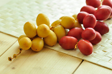 Fresh unripe Arabian date fruits. Red and yellow color sweet young dates placed on wooden matt.