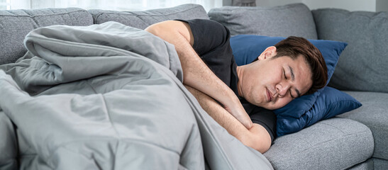 Asian man is lying with blanket on couch at home to rest when feeling sick from high fever, migraine