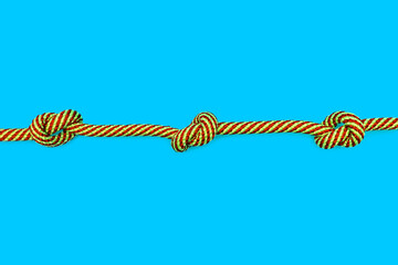 Multicolored rope with three knots on a blue background. Strong yellow-red rope with knots in the...