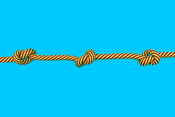 Multicolored rope with three knots on a blue background. Strong yellow-red rope with knots in the center of a blue background with free space for advertising or text